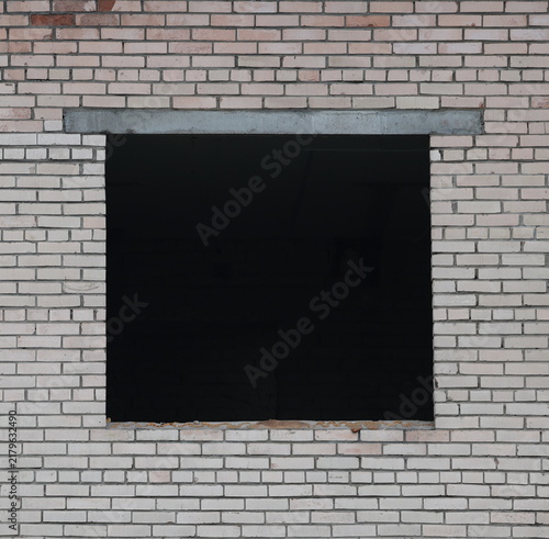 A square window opening without a window frame in a wall made of white brick