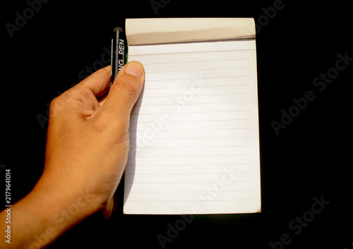 Close up of hand holding notepad with pen isolated on black background