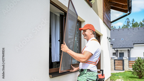 Worker installing mosquito wire screen on house window to protect from insects.