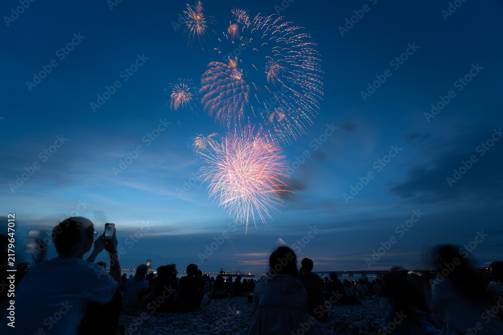 Obraz premium Fireworks bursting above spectators on an Osaka beach at dusk