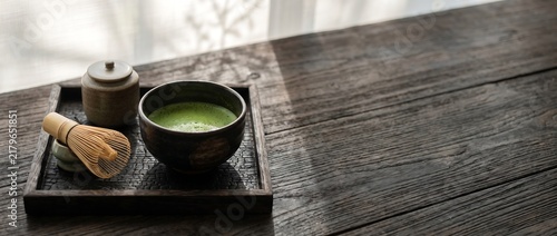 Fresh organic matcha green tea in a ceramic bowl with bamboo whisk on wooden table