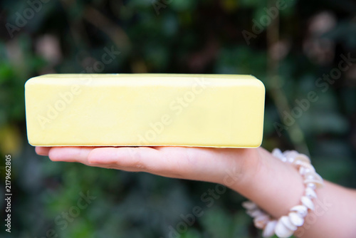 child hand holding yellow antistress butter slime toy shaped like stick of butter outdoors