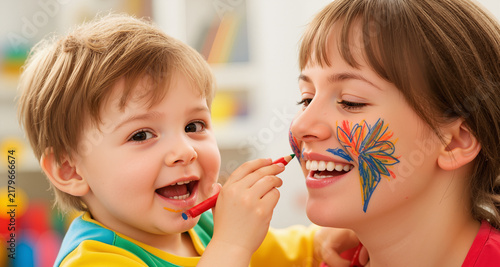 A cheerful child is drawing on their mom's face.