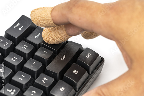 Close-up macro shot of bandaged and injured fingers pressing the enter key on a black computer keyboard, symbolizing the hidden risks and consequences that follow every click or keystroke