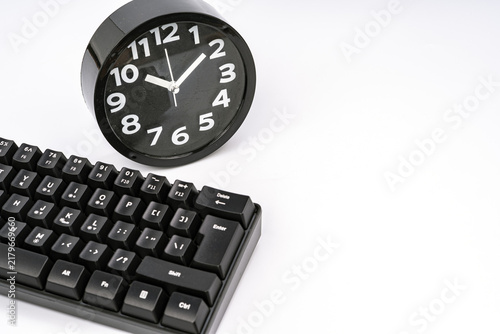 Close-up of a black round alarm clock positioned next to a mechanical computer keyboard on a white background, symbolizing time management, deadlines, efficiency, and productivity in digital work