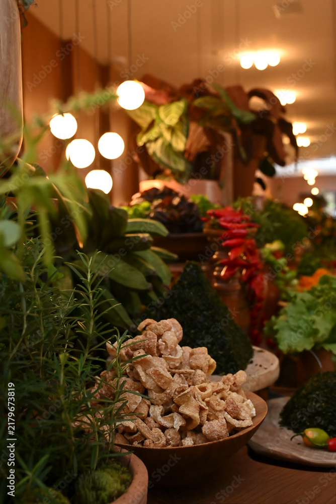 Fototapeta premium crispy Brazilian torresmo pork rinds piled on round wooden plate with fresh potted herbs for feijoada catering buffet, food setup close up horizontal shot