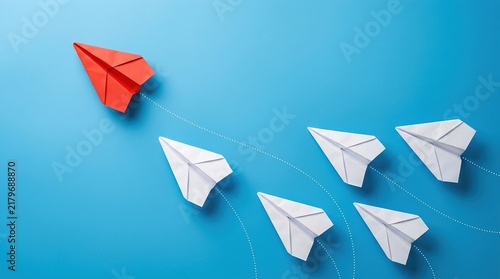 Single red paper plane leading group of white paper planes on bright blue background symbolizing leadership innovation and unique business strategy for market success.