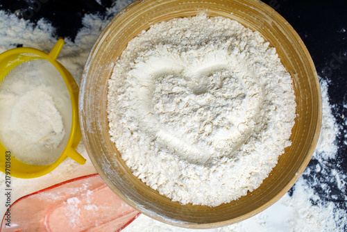 Cuadro en lienzo Heart shape drawn in a bowl of white flour beside a yellow sieve and pink scoop