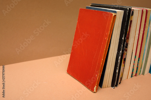Quadro su tela Stack of old books with a red cover standing on a beige background, perfect for