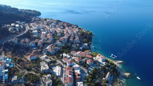 Aerial view of a Croatian seaside village with red-roofed houses, a curving shoreline, and calm blue Adriatic water.