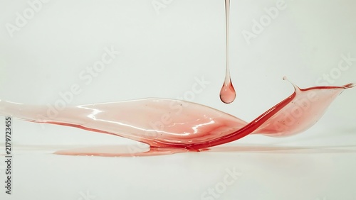 A delicate, translucent splash of red liquid forming a graceful wave shape on a light background, with a single, droplet suspended in, mid-air above.