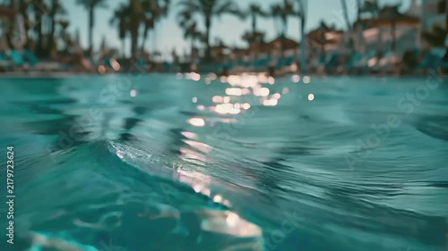 Summer hot vibe lifestyle. A vivid, closeup shot of a swimming pool at sunset. The water is a deep turquoise, reflecting the warm, golden light of the setting sun.