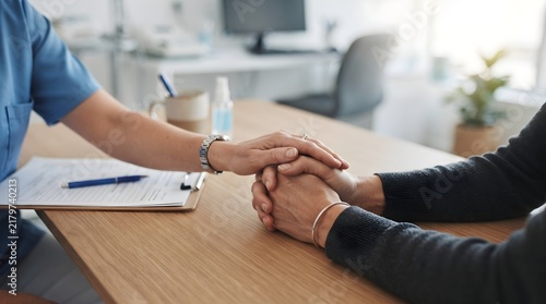 Physician Gently Holding Worried Patient's Clasped Hands at Clinic Desk