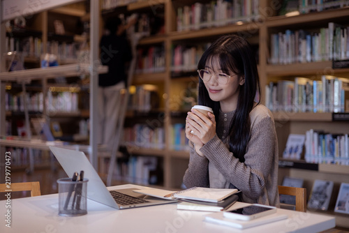 Принти на полотні Young Asian Woman Studying Freely in Library with Laptop and Coffee, Enjoying Ac