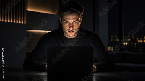 Laptop illuminating determined face in dark room, emotional breakthrough
