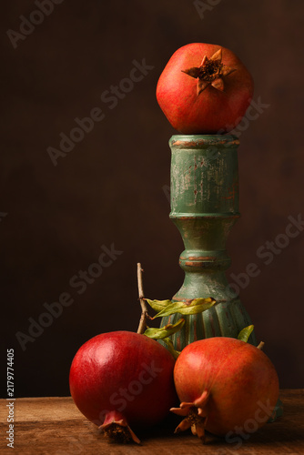 Pomegranate Still Life. Three ripe pomegranates around a greem pedestal with one on top.