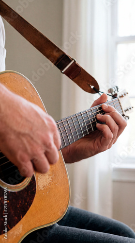 Musician fingers press guitar strings along weathered wooden fretboard