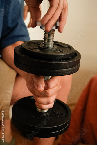 Person adjusting weights on adjustable dumbbell for strength training