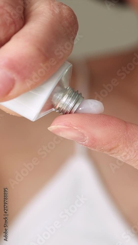 Woman Applying ointment from White Tube on Finger – Skincare, Treatment, Dermatology, Close-Up of Hands with Soft Focus Face in Background	