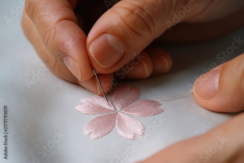 Skilled master hands embroidering a delicate pink flower petal motif on fabric with a fine needle and thread
