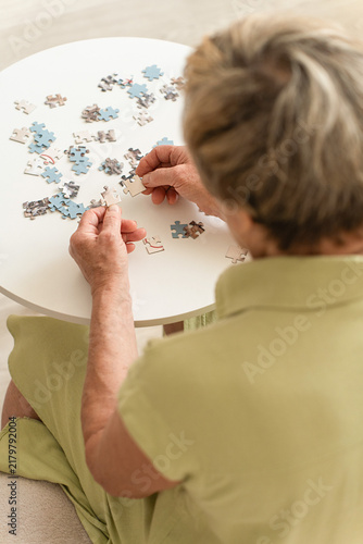 Elderly woman hands working on puzzle engage in mental and brain training to prevent dementia. Cognitive exercises for mental stimulation in older adults
