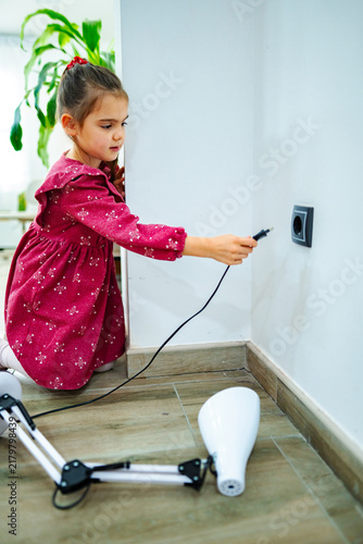 Foto Little girl plugging a lamp into a wall socket