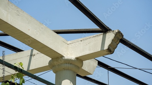 Fotografie Architectural detail of a concrete column joint with horizontal crossbeams and dark metal framework under bright sunlight and blue sky