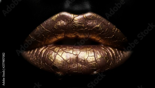 Close-up of golden cracked lips on a dark background, showcasing textured and artistic makeup