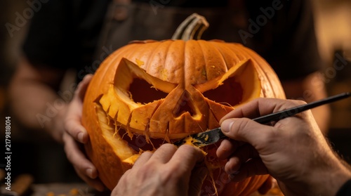 Close-up of hands carving a scary face into a pumpkin for Halloween decoration