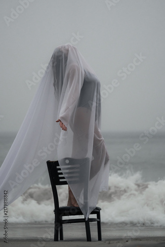 Фотография Person stands on a chair with a sheer cloth at the beach during a gray day