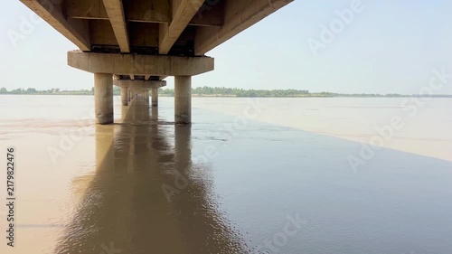 A close-up view of a vast river filled with flowing water and natural surface eddies, as it flows calmly beneath a sturdy bridge. 4k video