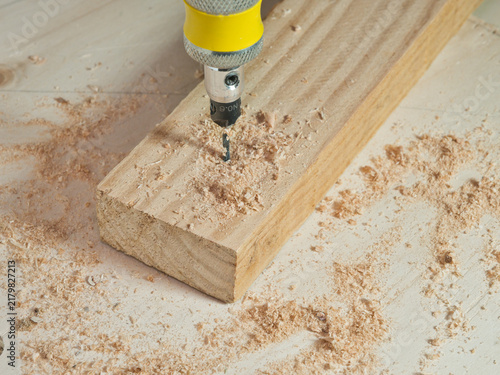 Fotografía Drilling into Wood Plank with Sawdust - A close-up shot captures a drill bit actively boring into a wooden plank, surrounded by fresh sawdust from the ongoing work