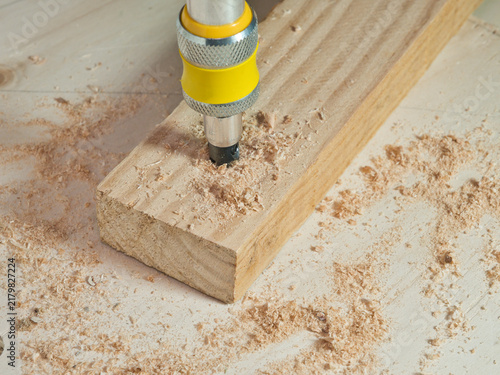 Konstfotografi Drilling into Wood Plank with Sawdust - A close-up shot captures a drill bit actively boring into a wooden plank, surrounded by fresh sawdust from the ongoing work