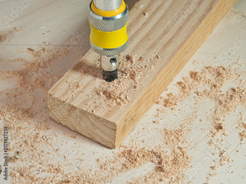 Fotografie Drilling into Wood Plank with Sawdust - A close-up shot captures a drill bit actively boring into a wooden plank, surrounded by fresh sawdust from the ongoing work