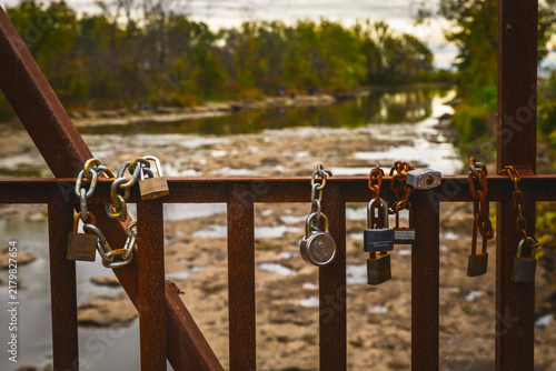 Fotografía Rusting love padlocks and chains on a steel bridge railing above a rocky river, Ontario, Canada