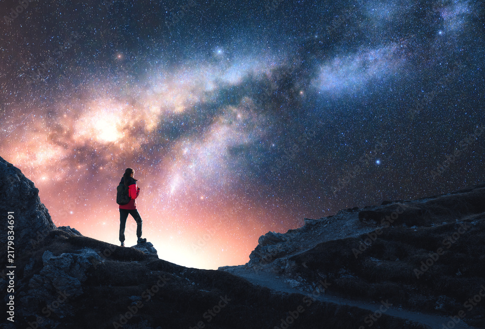 Fototapeta premium Glowing Milky Way and woman on mountain peak at starry night. Dolomites, Italy. Galaxy. Space landscape with silhouette of a girl, rocks, sky with bright stars. Milky Way and hiker. Nightscape