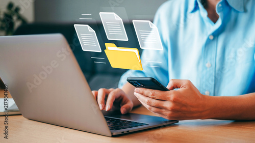 A professional managing digital documents and folders on a modern laptop and smartphone in a contemporary remote workspace environment