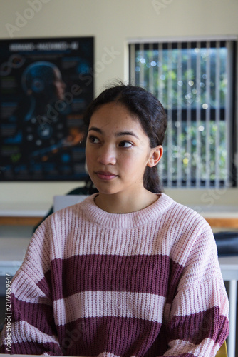 Foto Adolescent female sitting at classroom desk wearing chunky striped sweater, stud