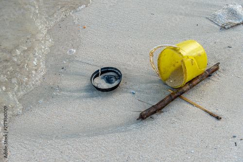 Obraz na plátně Intricate water patterns in the sand surround an abandoned black beverage lid and a cracked yellow bucket, capturing the persistence of microplastics on seashores