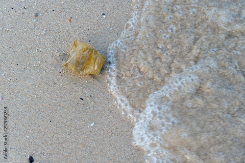 Fotografía A piece of discarded yellow plastic litter sits on wet sand as sea foam approaches, highlighting the ongoing issue of marine pollution on coastal shores