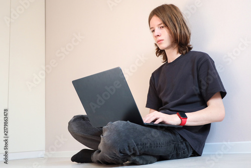 Young Person Sits Cross-Legged On Floor With Laptop, Working Or Browsing At Home In Bright Minimal Room. Additional Visual Context For Commercial. Additional Visual Context For Teenager