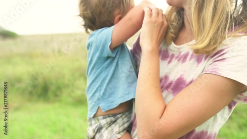 Toddler playfully grabbing his mother's arm during a close-up moment in a summer field