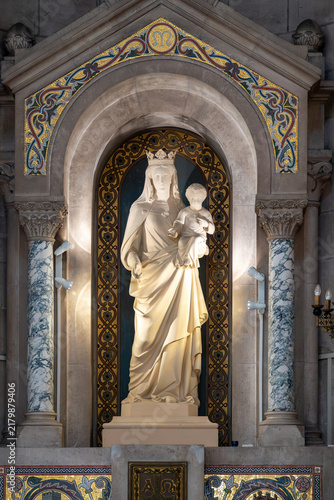 Quadro su tela A marble statue of the Virgin Mary holding child Jesus stands inside a decorated alcove