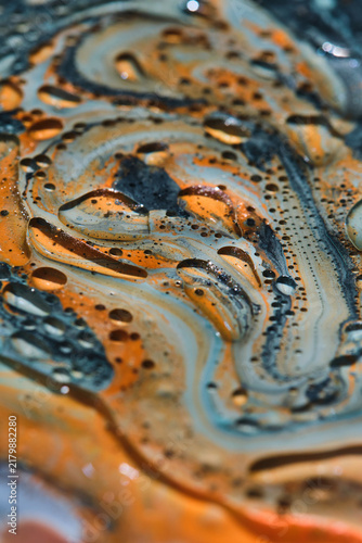 Vertical macro shot of swirling orange, light blue, and black paint with clear oil cell bubbles.