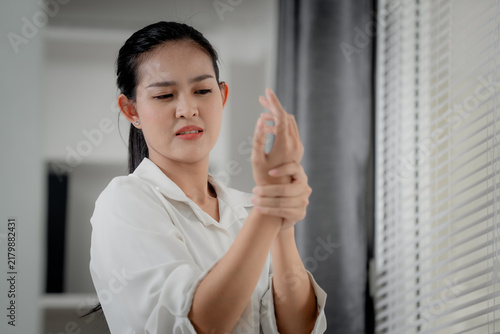 Office syndrome and wrist pain concept showing a woman holding her sore wrist indoors with a painful expression from repetitive strain. wrist, pain, office, strain, healthcare