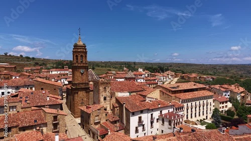 Panoramic view of La Iglesuela del Cid, a medieval village in Teruel, Aragon, Spain, featuring a historic church clock tower and terracotta rooftops under blue sky