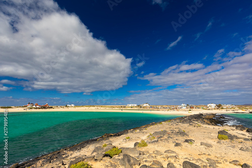 Panoramic view of a volcanic beach and the turquoise Atlantic Ocean under a blue sky on Fuerteventura (Canary Islands) – a background or wallpaper for your project