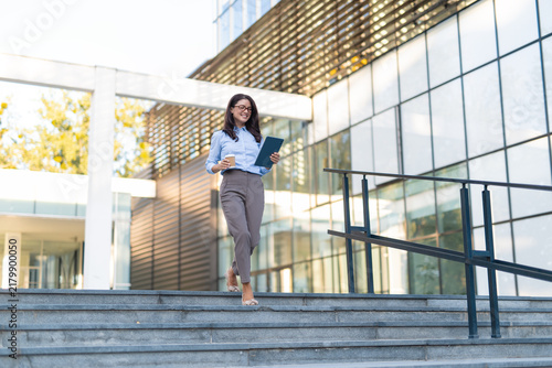 Konstfotografi Businesswoman walking downstairs holding tablet and coffee