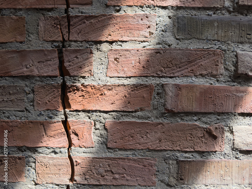 Cracked red brick wall texture with natural sunlight and shadows