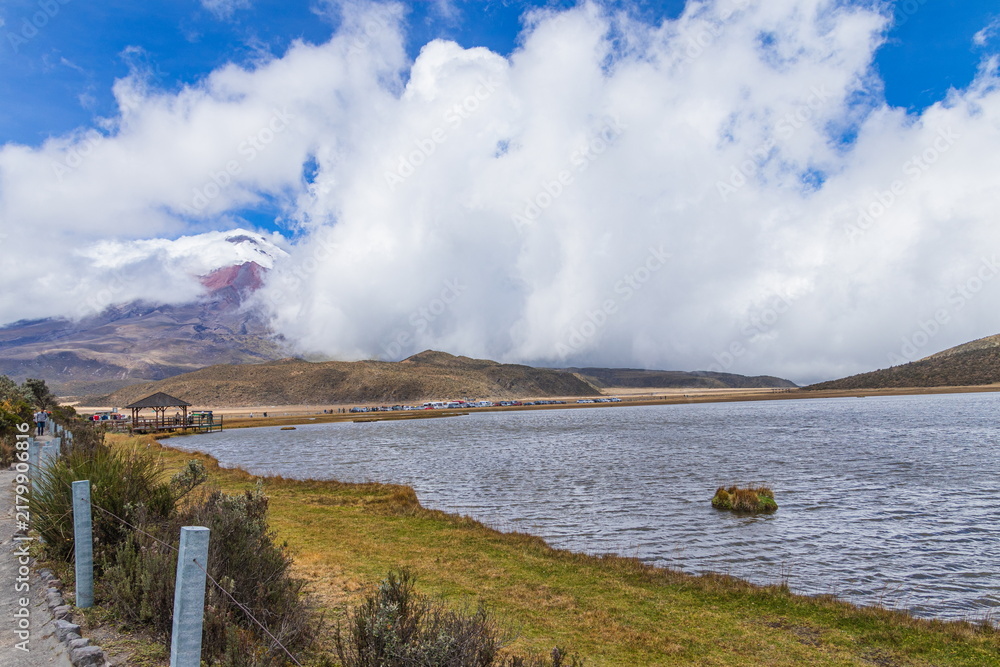Obraz premium A beautiful panoramic view of the lake Limpiopungo and the majestic, snow-capped Cotopaxi active volcano partially covered by clouds in Cotopaxi National Park, Ecuador